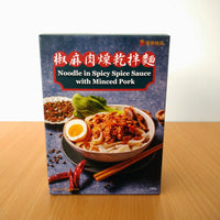 A box of 'Minced Pork Noodles with Chili Sauce' sits on a wooden surface. The ready-to-eat packaging is printed with images of the dish showcasing the noodles, minced pork, poached egg and garnish. Red and gold text on a dark background and food illustrations complete the look.