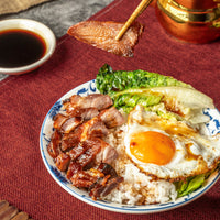 A bowl of rice topped with Plum Sauce Glazed Char Siu, fried egg and steamed bok choy with soy sauce.