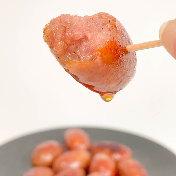 Close up shot of cooked juicy Taiwan Cocktail Sausage (Mini Sausage) on sticks with a drop of sauce dripping from them, blurred background with more Taiwan Cocktail Sausage (Mini Sausage)on a gray plate in the background.