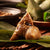 Close-up of a bamboo leaf wrapped dumpling filled with ingredients such as meat and nuts, this dumpling rests on an open leaf with additional bamboo leaves and a plate in the background, chestnut mushrooms add a savory flavor to the traditional Taiwanese dumplings.